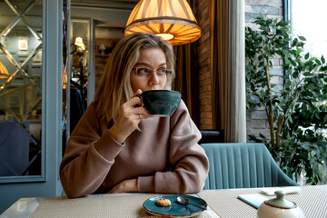 Middle-aged blonde caucasian woman drinks coffee in cafe