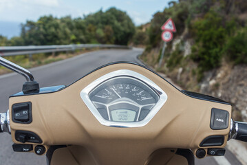 View of the winding road from behind the steering wheel of a scooter. Biker driving his motorcycle on country road in a village. Point of view with focus is on the handlebar