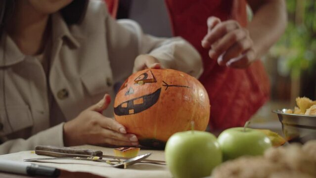 A young man is watching how his friend is carving a pumpkin for Halloween