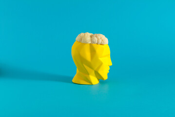 Minimal concept yellow sculpture head with cauliflower. Creative concept on blue background.