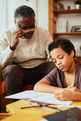 An African-American grandfather is sitting at home with his grandson and helping him with homework.
