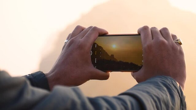 Close up of Male hands using smartphone and clicking photos of Girnar mountain. Photographer Creating multimedia content of mountains during sunrise, man clicking pictures during trekking adventure.