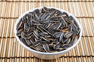 Black sunflower seeds in a bowl on wooden background