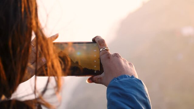 Close up of Female hands using smartphone and clicking photos of Girnar mountain. Photographer Creating multimedia content of mountains during sunrise, woman clicking picture during trekking adventure