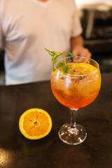 fruit cocktail next to half an orange, bartender in the background