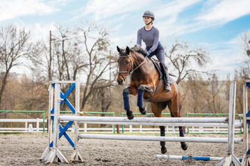 Equestrian sport. Show jumping competition. Young rider horseback girl jumping over an obstacle on...