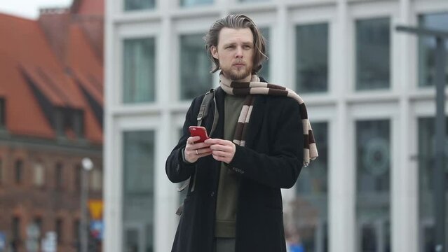 stylish guy in scarf and coat hold mobile phone in a hand at street of Wroclaw, Poland