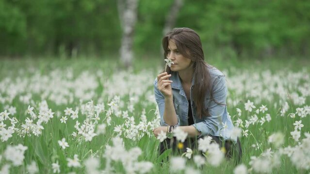 Portrait of beautiful woman smelling a flower in blossom white daffodils field