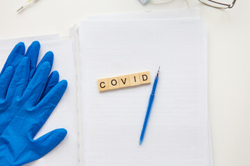 The inscription covid on a medical background, next to gloves, a pen, glasses and papers with patient data. Medical theme. Concept: vaccination against coronavirus.