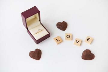 The inscription in wooden letters love, small truffle sweets in the form of a heart. Diamond ring box - marriage proposal.