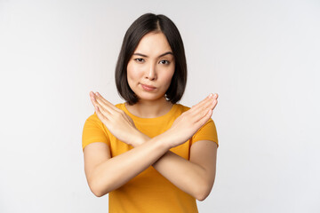 Portrait of asian woman looking serious and angry, showing stop prohibit gesture, taboo sign,...
