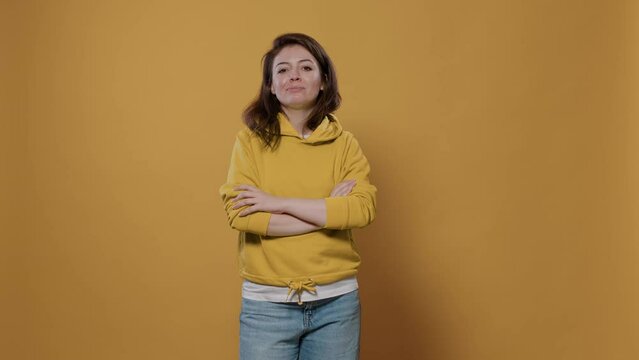 Portrait of smiling caucasian woman posing confident with arms crossed, feeling confident and proud in studio. Happy young person looking succesful and pleased with big smile over yellow background.