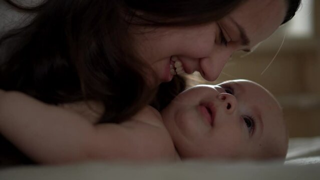 Newborn Baby With Young Mom look Into Each Other Eye. Cute Smiling Teethless Kid Face Portrait. Woman Kissing With Child Look At Camera. Infant, Mother Day, Childbirth, Beginning, Relationship Concept