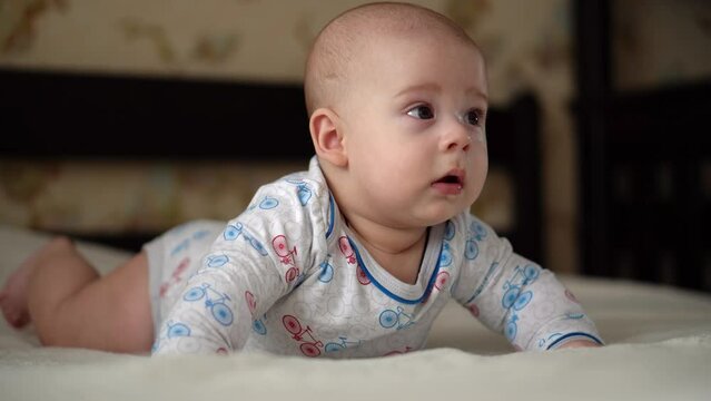 Newborn Active Baby Cute Smiling Teethless Face Portrait Early Days On Stomach Developing Neck Control. 5 Months Child On White Bed Looking on Camera. Infant, Childbirth, Parenthood, Beginning Concept