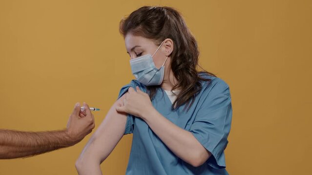Portrait of medical doctor wearing surgical mask lifting sleeve and recieving covid or flu vaccine in studio. Medic wearing corona virus protection getting immunization shot from syringe.