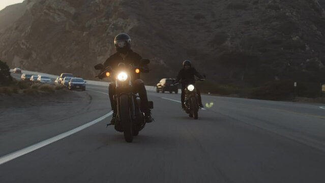 Close-up shot of bikers riding on a highway at sunset. Idyllic landscape of the coastal area with steep rocky cliff in the background as seen from a motorway. High quality 4k footage