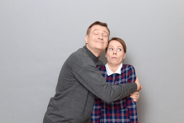 Shot of funny couple, happy cheerful man is hugging shocked woman