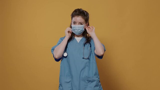 Woman doctor putting on surgical mask for protection against corona virus for covid pandemic awerness campaign. Portrait of caucasian medic wearing protective uniform and stethoscope.