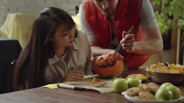 A young man teaches a lady how to carve eyes for a halloween pumpkin