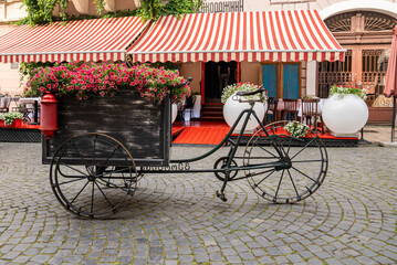 Kyiv, Ukraine. July 20, 2021. Vintage style three wheeled bicycle carriage with beautiful flower arrangement in front of outdoor cafe