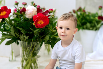 A little boy in a white T-shirt with blooming peonies. Spring. A child in flowers.