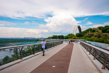 Kyiv, Ukraine. July 20, 2021. Tourists on pedestrian and bicycle bridge connecting to Saint Volodymyr Hill and the monument of Peoples' Friendship Arch