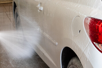 Car wash. Powerful jet of white foam applied on white car in open garage