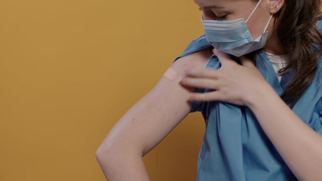 Closeup of medical doctor wearing surgical mask lifting sleeve and recieving band aid after covid or flu vaccine in studio. Detail view of medic getting bandage from male nurse after immunization.