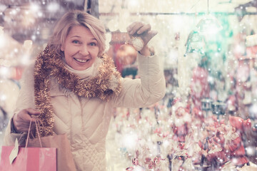 Portrait of happy mature woman in tinsel with Christmas toys at fair outdoor.