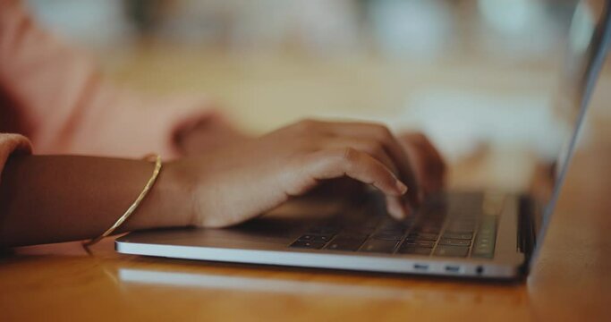 Black woman typing on keyboard on laptop in coffee shop