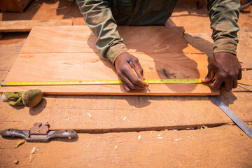 Close-up of the hands of an African carpenter who is taking measurements to cut a piece of wood to...