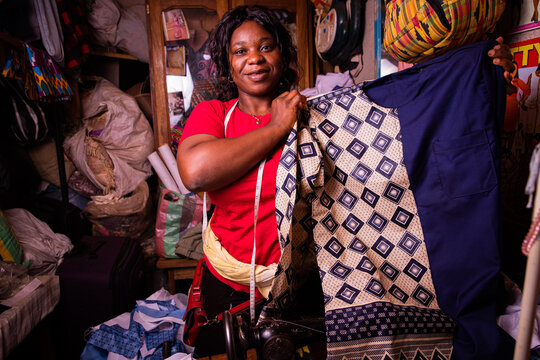 A happy African seamstress shows off the dress she has just finished sewing. Typical African suit for men just made