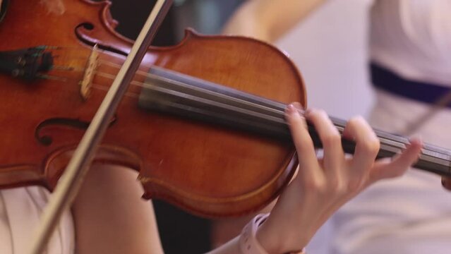 Violin player, fiddler violinist with a bow performing music on stage during concert with orchestra and musical band in the background
