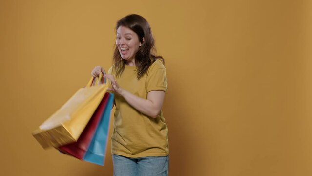 Smiling woman holding shopping bags feeling ecstatic and pleased with purchase doing thumb up hand gesture in studio. Person feeling proud of aquisition showing excitement for buying products.