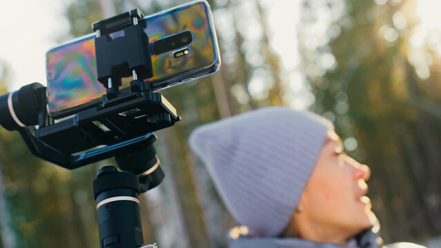 The Woman Professional Videographer Holding Smartphone on 3-axis Gimbal Stabilization Device in Winter. Pro Equipment Helps to Make High Quality Video on Phone. Cinematographer Operator. Slow Motion