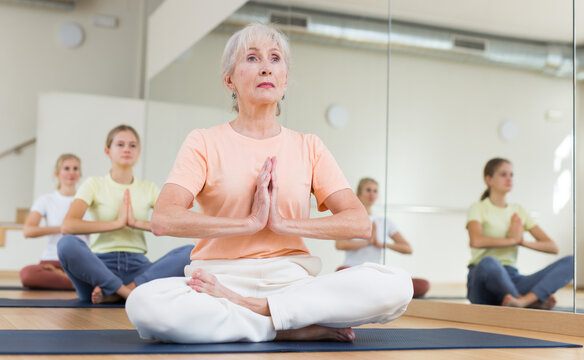 Group of people of different ages sitting in lotus position practicing meditation in yoga class - Powered by Adobe