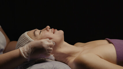 Young hypnotic face woman receiving anti-ageing facial massage in spa salon relax. Wellness body...