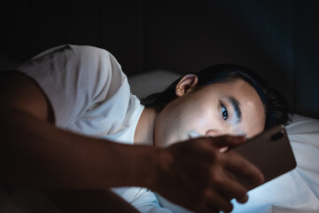 Young man lying on the bed using mobile phone in the dark 