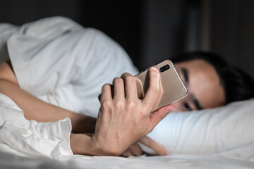 Young man lying on the bed using mobile phone in the dark 