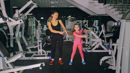 Fototapeta na wymiar Mother and Daughter in the Gym, Family Performs Physical doing Exercises Fitness, Healthy Lifestyle. Happy Sports Family Training Concept. Woman with her Child doing Stretching Warm-up in the Gym