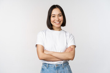 Portrait of happy asian woman smiling, posing confident, cross arms on chest, standing against studio background - Powered by Adobe