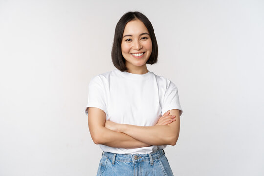 Portrait of happy asian woman smiling, posing confident, cross arms on chest, standing against studio background