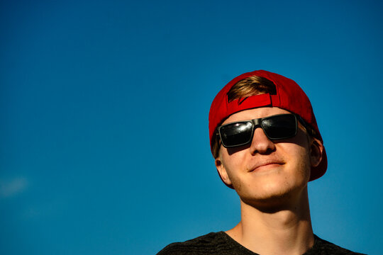 Portrait of a young man wearing sun glasses and a red cap under the sunny blue sky