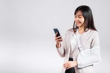 Fototapeta premium Woman confident smiling broken arm after accident and wear arm splint for treatment and hold smartphone, happy Asian female sling supported hand isolated on white background, social media, copy space