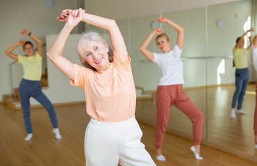 Positive mature woman doing aerobics exercises with group of people in dance center