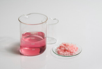Close up inorganic chemical on white laboratory table. Pink flake chemicals in Chemical Watch Glass...