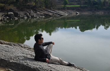 Man sitting near lake shore on huge rock relaxing and looking at view