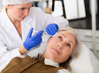 Closeup portrait of aged woman getting injections for face skin tightening at aesthetic cosmetology...