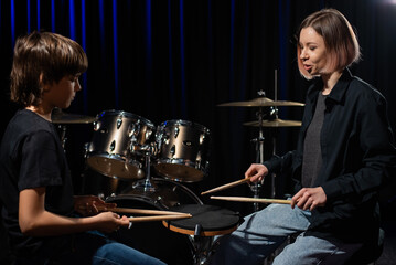 Fototapeta na wymiar Young caucasian woman teaches a boy to play the drums in the studio on a black background. Music school student