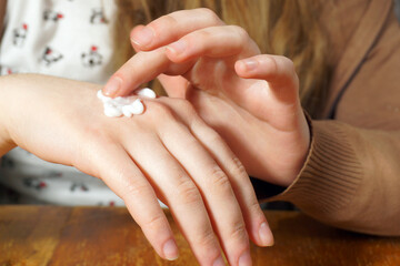 Woman's fingers applying cosmetic cream to her hands.